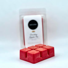 Load image into Gallery viewer, Red wax melts in a rectangular tray in the foreground, with their clear plastic packaging and white label card blurred in the background on a white surface.
