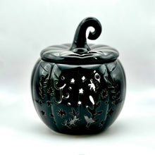 Load image into Gallery viewer, A black ceramic pumpkin-shaped wax melt burner with a lid and a curved handle, featuring white cutout floral and star patterns, set against a white background.
