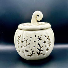 Load image into Gallery viewer, An off-white ceramic pumpkin-shaped wax melt burner with a lid, featuring decorative cutouts of stars, leaves, and swirls, set against a dark gray background. 
