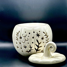 Load image into Gallery viewer, An off-white ceramic pumpkin-shaped wax melt burner with leaf and star cutouts, shown with its matching lid on a dark reflective surface.
