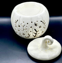 Load image into Gallery viewer, A white ceramic pumpkin-shaped wax melt burner with a matching lid, featuring laser-cut star and leaf patterns on the body, displayed on a dark reflective surface.
