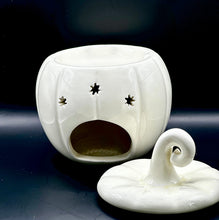 Load image into Gallery viewer, A white ceramic pumpkin-shaped wax melt burner with star-shaped cutouts and a matching lid featuring a curled handle, displayed on a dark surface against a dark background.

