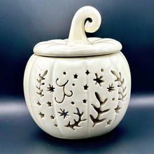Load image into Gallery viewer, An off-white ceramic pumpkin-shaped wax melt burner with a matching lid and curled stem, featuring decorative cutout patterns of stars, leaves, and abstract shapes, displayed on a dark surface against a dark background.
