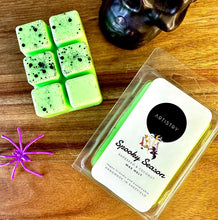 Load image into Gallery viewer, A packaged wax melt set on a wooden surface next to three mint green wax cubes with black speckles, a purple spider decoration, and a dark skull figurine. The package label reads 'ARTISTRY' and 'Spooky Season'.
